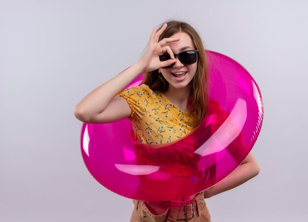 Joyful young girl wearing sunglasses and swim ring doing look gesture on isolated white space with copy space