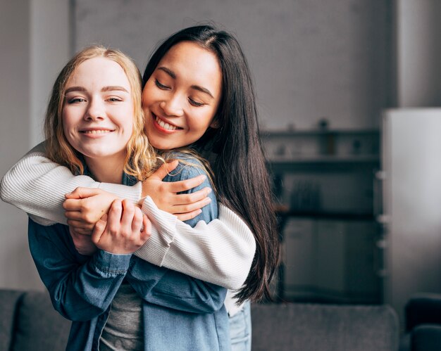 Joyful young girlfriends cuddling at home