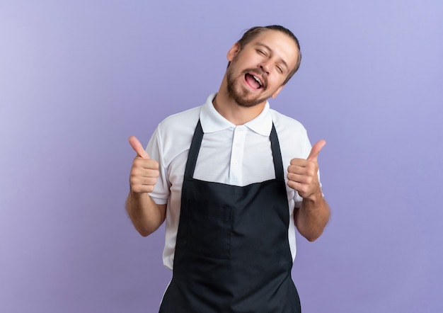 Joyful young handsome barber wearing uniform showing thumbs up with closed eyes isolated on purple