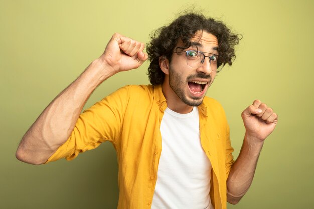 Joyful young handsome caucasian man wearing glasses  doing yes gesture isolated on olive green wall