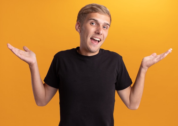 Free photo joyful young handsome guy wearing black shirt spreading hands isolated on yellow wall