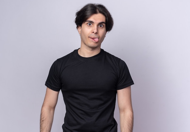 Joyful young handsome guy wearing black t-shirt showing tongue isolated on white wall