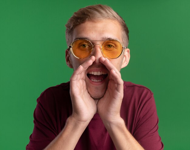 Joyful young handsome guy wearing red shirt and glasses - isolated on green wall