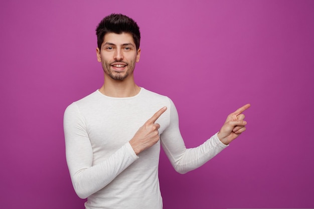 Joyful young handsome man looking at camera pointing to side on purple background