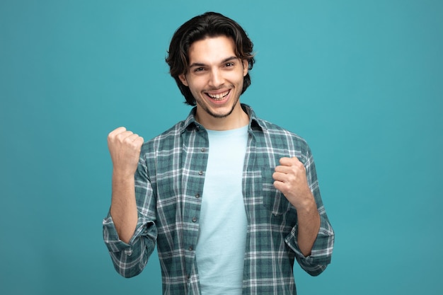 joyful young handsome man looking at camera showing yes gesture isolated on blue background