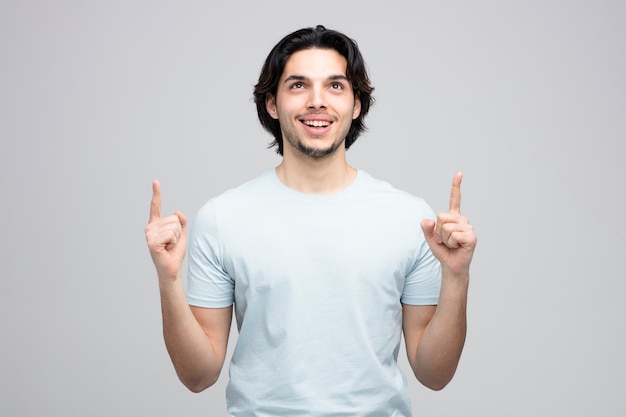 Joyful young handsome man looking up pointing fingers up isolated on white background