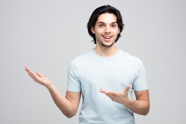 joyful young handsome man showing empty hands while looking at camera isolated on white background