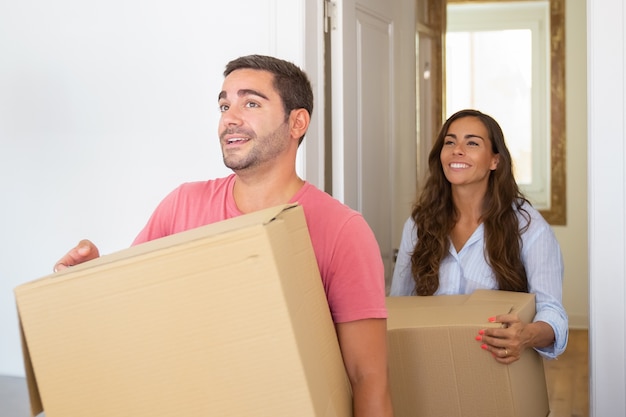 Радостная молодая латинская пара приходит в свою новую квартиру с картонными коробками