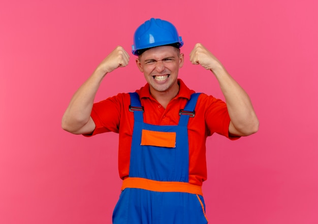 Foto gratuita giovane costruttore maschio allegro che indossa l'uniforme e il casco di sicurezza che mostra il gesto di sì