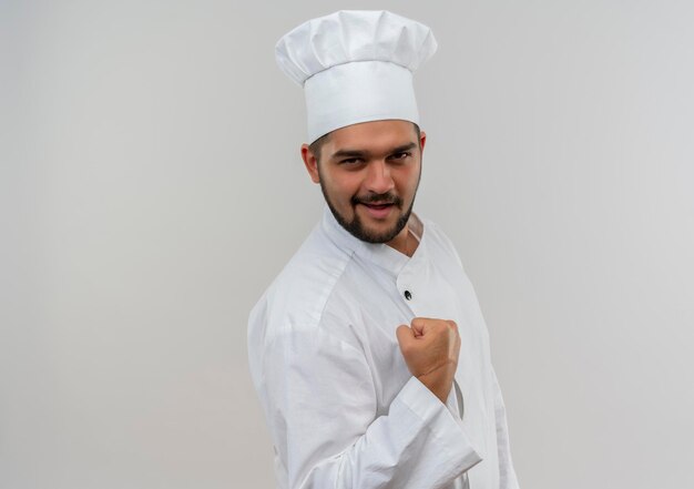 コピー スペースで白い壁に分離された拳を握り締めるシェフの制服を着たうれしそうな若い男性料理人