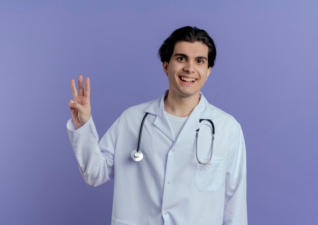 의료 가운과 청진기를 입고 즐거운 젊은 남성 의사 복사 공간 보라색 벽에 고립 된 평화 서명 하 고