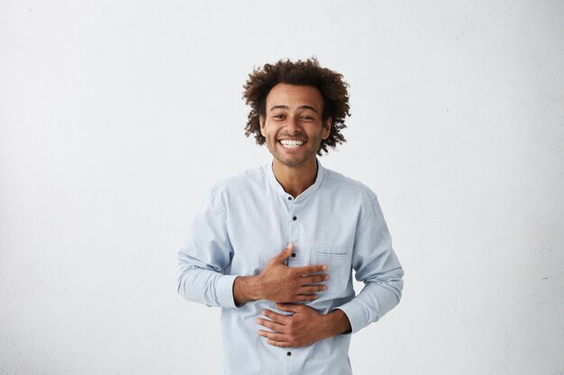 Free photo joyful young man holding hands on stomach while laughing out loud at something funny