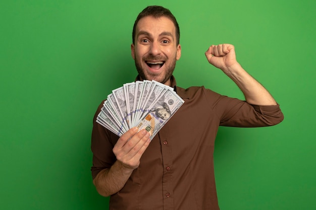 Free photo joyful young man holding money looking at front doing yes gesture isolated on green wall