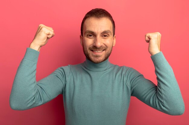 Joyful young man looking at front doing yes gesture isolated on pink wall