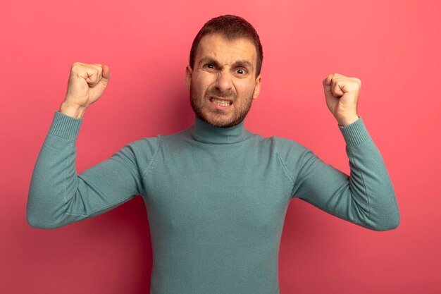 Joyful young man looking at front doing yes gesture isolated on pink wall