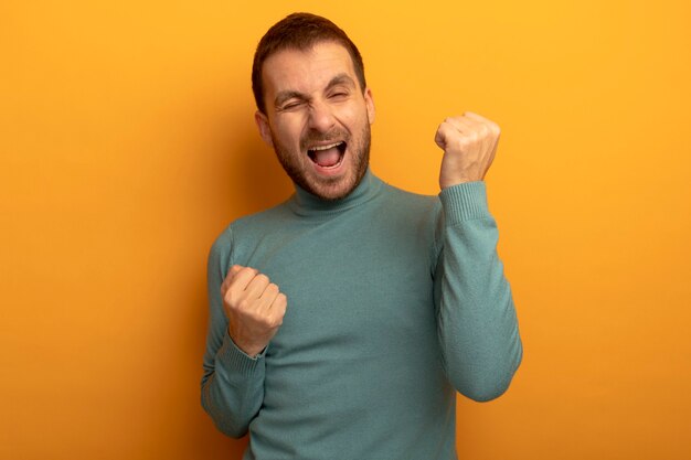 Joyful young man winking at front doing yes gesture isolated on orange wall