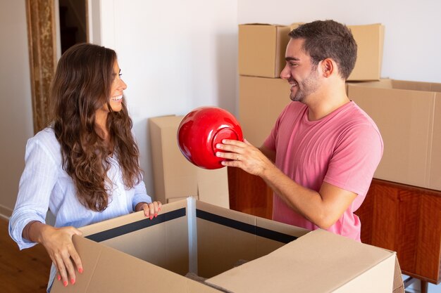 Joyful young man and woman moving and unpacking things, getting out object of open carton box