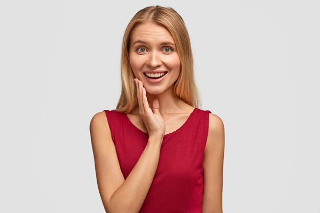 Joyful young pretty European woman with light straight hair, being in good mood