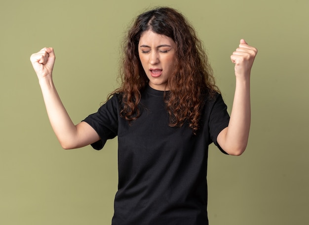 Joyful young pretty girl doing yes gesture with closed eyes isolated on olive green wall