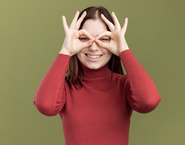 Foto gratuita gioiosa ragazza carina che indossa occhiali da sole che fa un gesto di sguardo usando le mani come binocolo