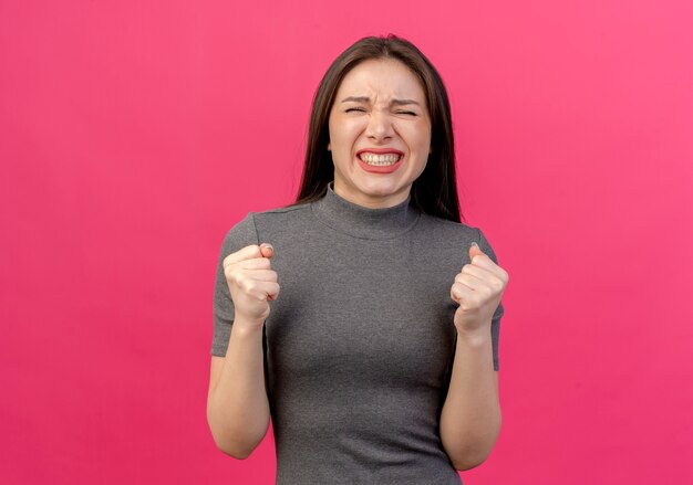 Joyful young pretty woman clenching fists isolated on pink background with copy space