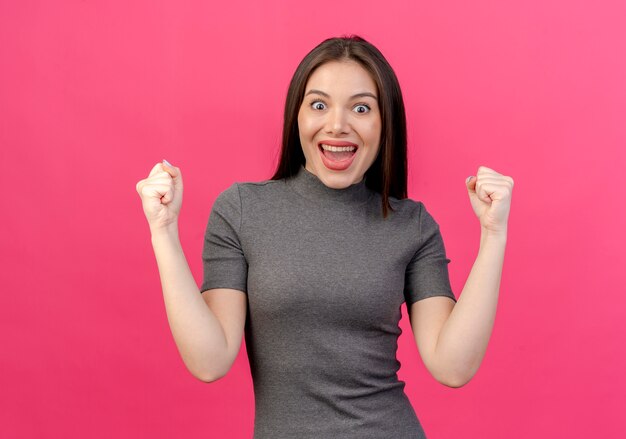 Joyful young pretty woman clenching fists looking at camera isolated on pink background