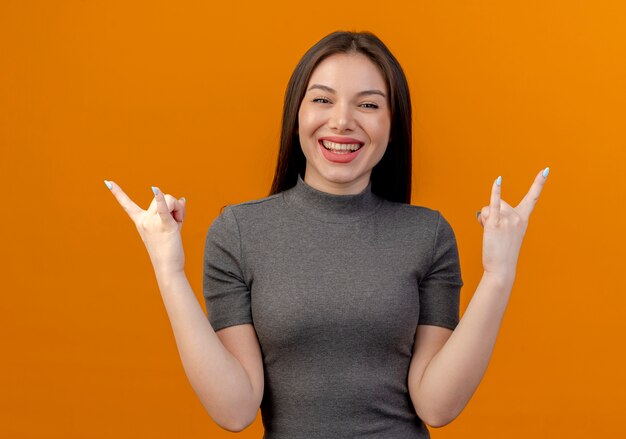 Радостная молодая красивая женщина делает рок знаки, изолированные на оранжевом фоне