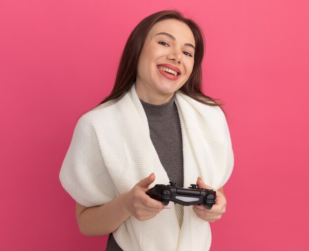 Joyful young pretty woman holding game controller joystick  isolated on pink wall