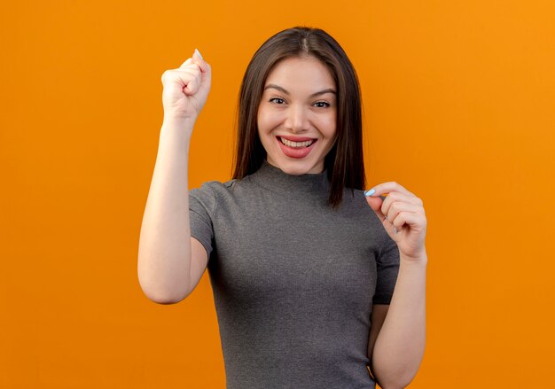 joyful young pretty woman raising fist isolated on orange