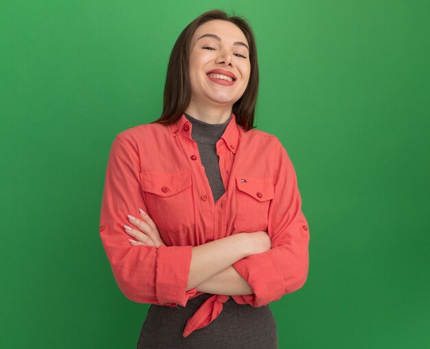 Joyful young pretty woman standing with closed posture  laughing isolated on green wall with copy space