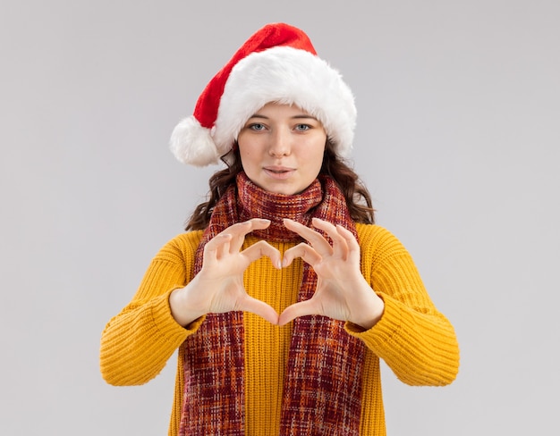 Foto gratuita gioiosa giovane ragazza slava con cappello santa e con sciarpa intorno al collo gesticolando segno di cuore