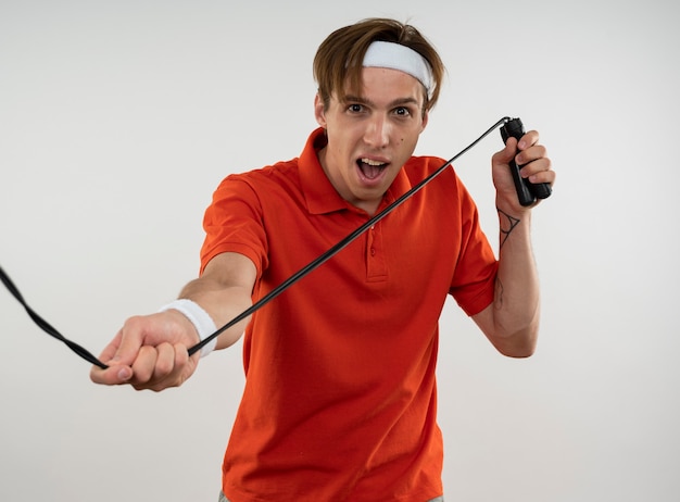 Joyful young sporty guy wearing headband with wristband stretching jump rope