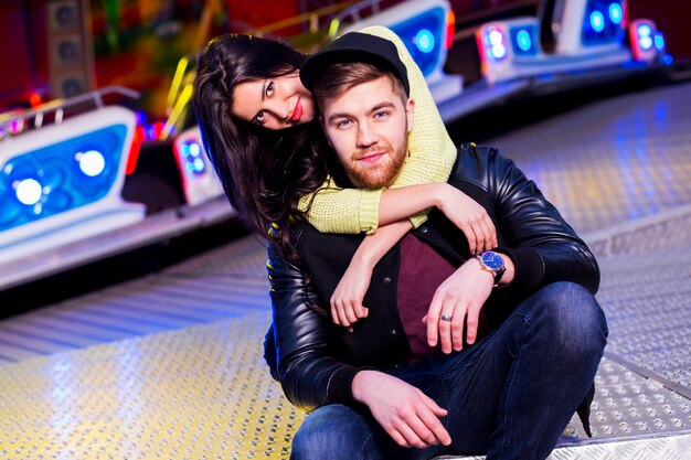 Joyful young stylish  couple being playful while visiting an attractions park arcade with rides