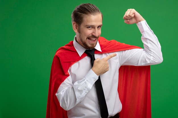 Joyful young superhero guy showing strong gesture isolated on green