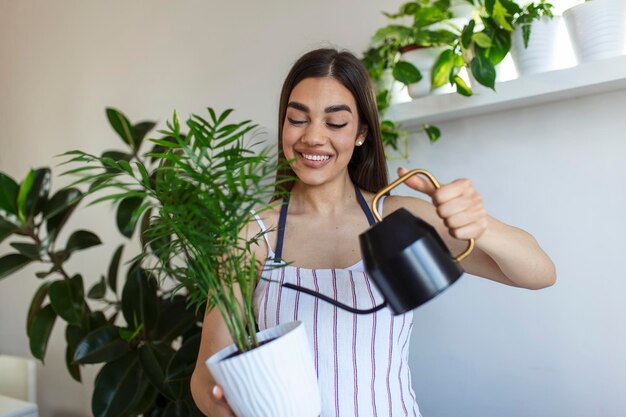 Joyful young woman enjoys her time at home and watering her plant by the window at home