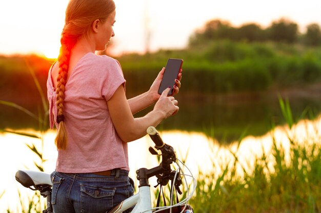 Радостная молодая женщина, едущая на велосипеде на набережной реки и луга.