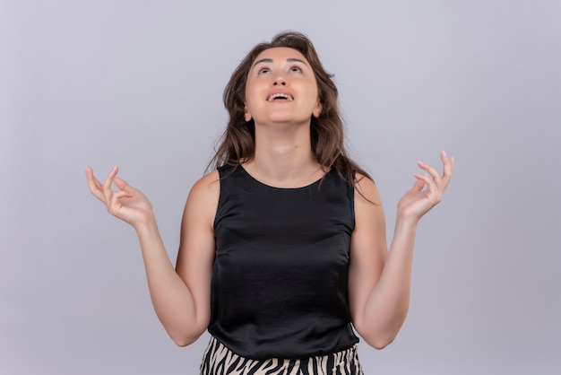 Free photo joyful young woman wearing black undershirt spreads hand on white wall