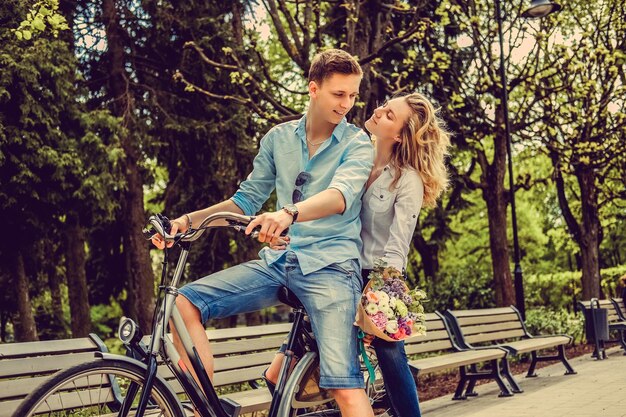 Joyfull couple posing on one bicycle in a city summer park.