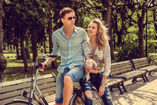 Joyfull couple posing on one bicycle in a city summer park.