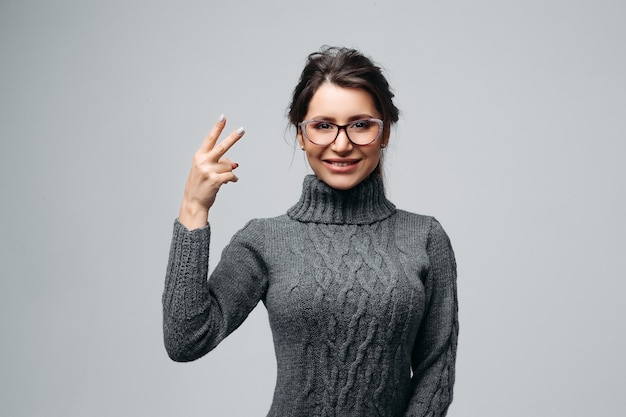 Joyous girl in glasses demonstrating victory sign