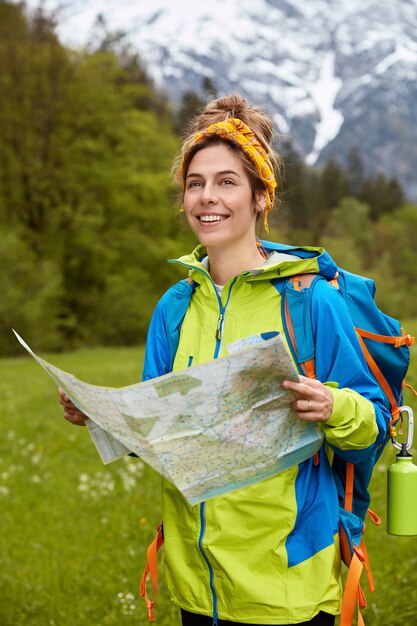 Joyous pleased young woman dressed casully, reads map, finds necessary location, considers route