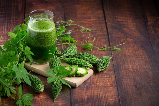 a jug of bitter gourd smoothie with raw bitter gourd put on wooden board