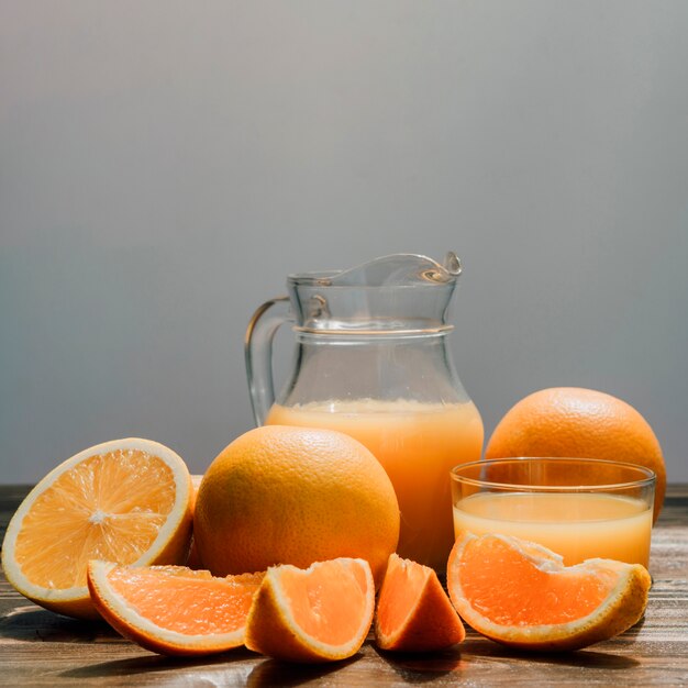 Jug of delicious orange juice surrounded by glasses and oranges