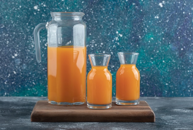 Jug and glasses of orange juice on wooden board. 