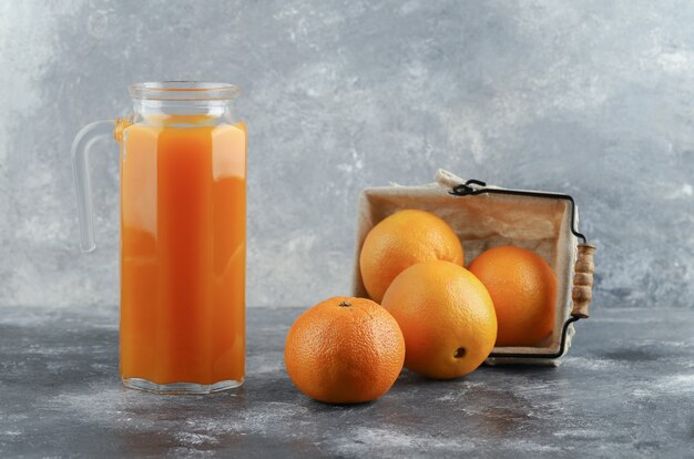 大理石のテーブルにジュースとオレンジのバスケットの水差し。