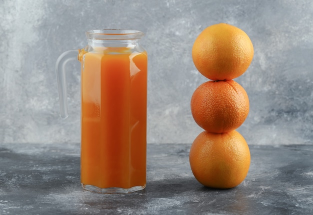 Jug of juice and oranges on marble table