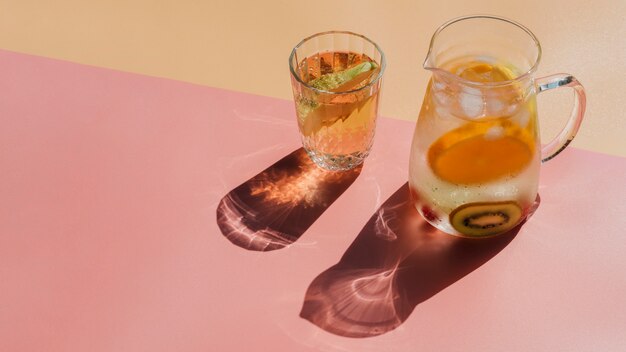 Jug and transparent glass filled with water and slices of fruits