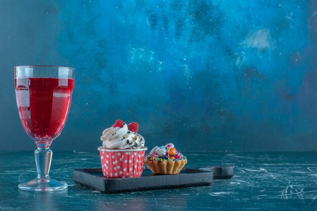 A juice glass next to cupcakes on blue background. High quality photo