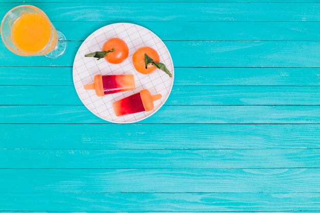 Juice and tangerines and popsicle on plate on wooden surface