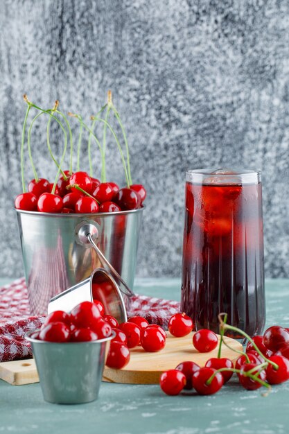 Juice with cherries, cutting board, kitchen towel in a jug, side view.